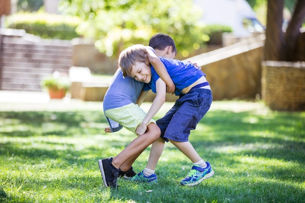 Zwei Jungen kämpfen draußen. Geschwister oder Freunde, die im Sommerpark ringen. Geschwisterrivalität.