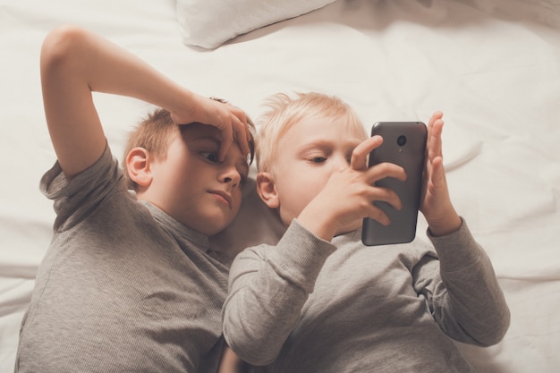 Zwei Jungen liegen mit einem Smartphone im Bett. Gadget Freizeit