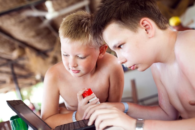 Foto zwei jungs spielen im urlaub in einer strandbar mit einem laptop