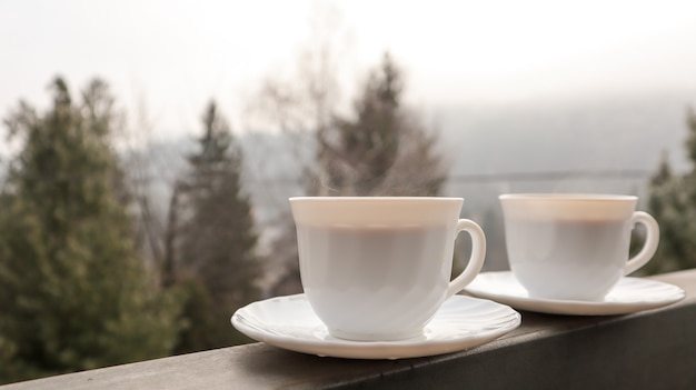 Zwei Kaffeetassen auf einem Balkon mit Berglandschaft am Morgen.