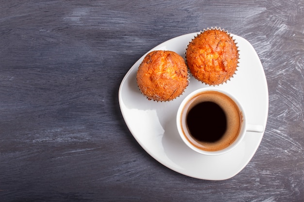 Zwei Karottenmuffins mit Tasse Kaffee auf weißer Platte auf schwarzem hölzernem Hintergrund