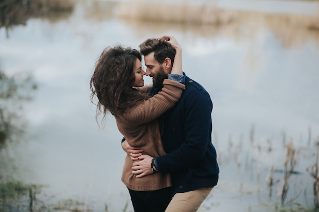 Foto zwei kaukasische liebhaber nahe dem see. junges paar umarmt am herbsttag im freien. ein bärtiger mann und eine verliebte lockige frau. konzept der liebe.