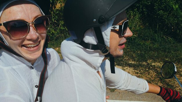 Zwei kaukasische touristische Frauen fahren auf rotem Roller. Machen Sie ein Selfie. Liebespaar auf dem Motorrad in weißen Kleidern, um auf Forststraßen-Trail-Trip zu gehen.