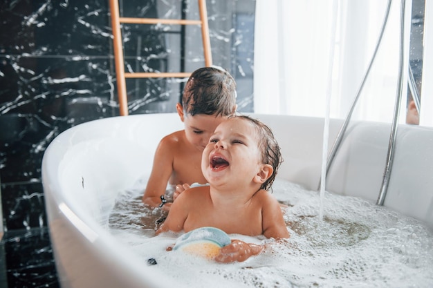 Zwei Kinder, die Spaß haben und sich zu Hause in der Badewanne waschen und sich gegenseitig helfen