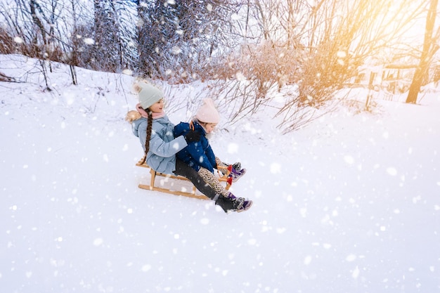 Zwei Kinder fahren an einem sonnigen Wintertag auf einem Retro-Holzschlitten