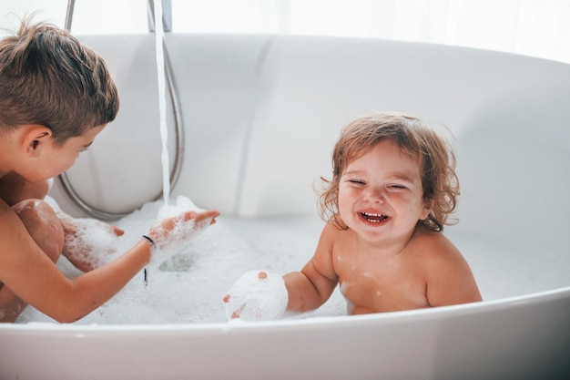 Zwei Kinder haben Spaß und waschen sich zu Hause in der Badewanne Posieren für eine Kamera