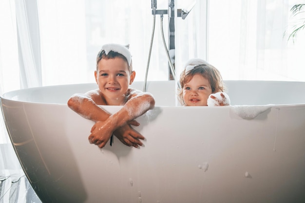 Zwei Kinder haben Spaß und waschen sich zu Hause in der Badewanne Posieren für eine Kamera