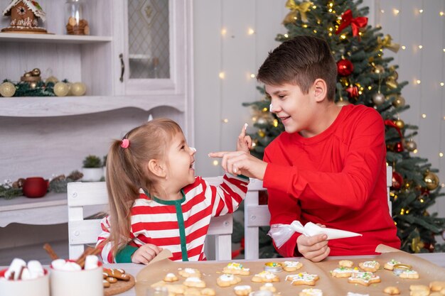 Zwei Kinder, Junge und Mädchen im Schlafanzug, kochen festlichen Lebkuchen in der weihnachtlich dekorierten Küche