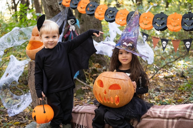 zwei Kinder Mädchen und Junge im Halloween-Kostüm mit Kürbissen in Halloween-Dekorationen im Freien