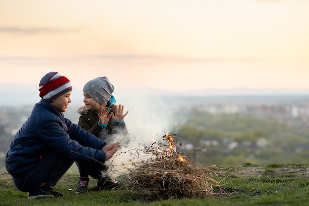 Zwei Kinder spielen bei kaltem Wetter mit Feuer im Freien.