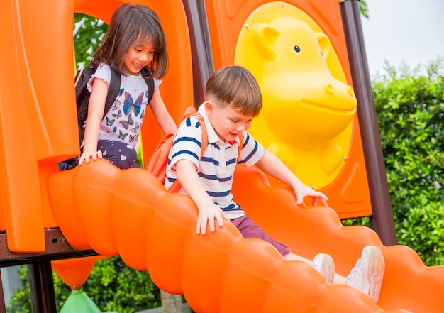 Zwei Kinderfreunde, die Spaß haben, zusammen auf dem Spielplatz der Kinder der Rutsche in der Schule zu spielen