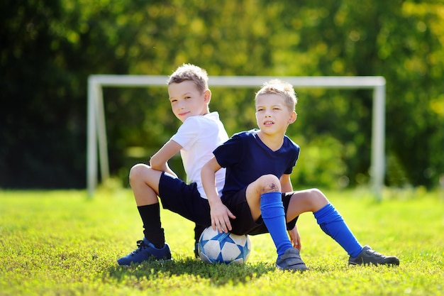 Zwei kleine Brüder, die Spaß haben, ein Fußballspiel am sonnigen Sommertag zu spielen