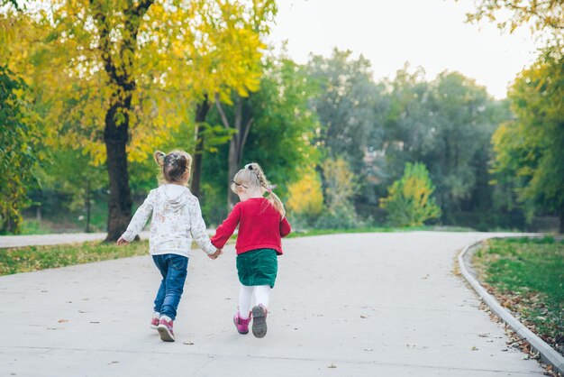 Zwei kleine Freundinnen spielen im Herbststadtpark Händchen haltend