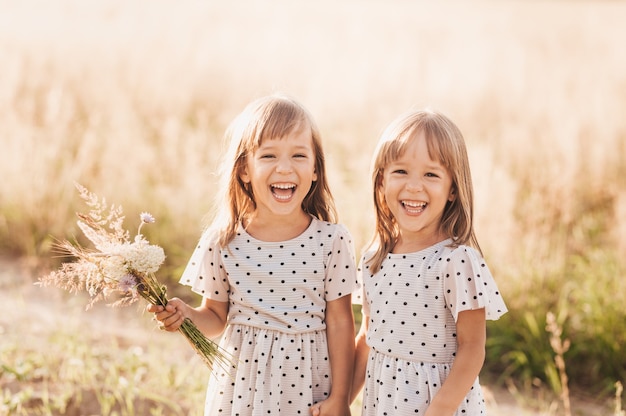 Zwei kleine glückliche eineiige Zwillingsmädchen, die im Sommer zusammen in der Natur spielen. Mädchenfreundschaft und Jugendkonzept. Aktiver Lebensstil der Kinder.