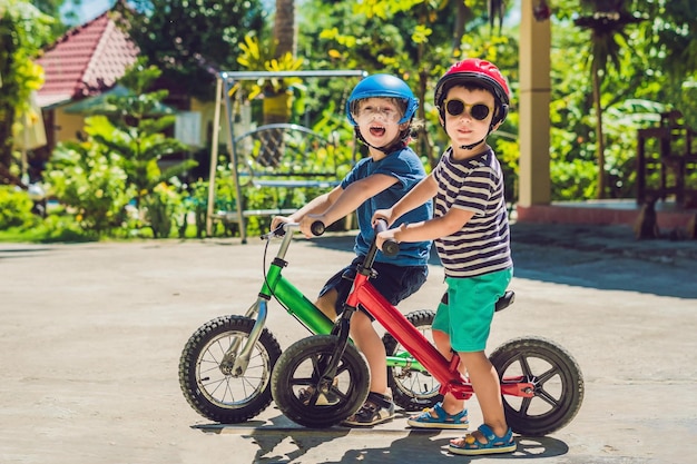 Zwei kleine Jungen, die Spaß auf dem Laufrad auf einer tropischen Landstraße haben.