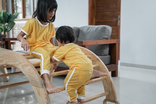 Zwei kleine Kinder, die in Pikler-Dreiecksspielzeug im Wohnzimmerhintergrund spielen