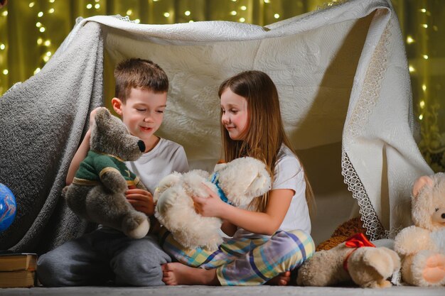 Zwei kleine Kinder spielen abends zu Hause, um ein Campingzelt zu bauen, um Bücher mit einer Taschenlampe zu lesen und drinnen zu schlafen Konzept der magischen Kreativitätsalarmsysteme des Spiels