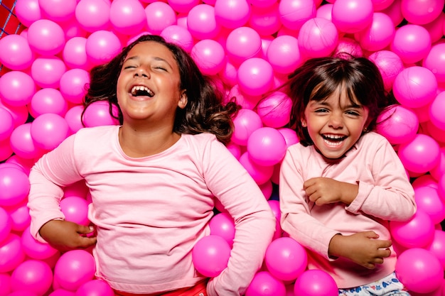 Zwei kleine Mädchen, die am rosa Ballpool lächeln und spielen