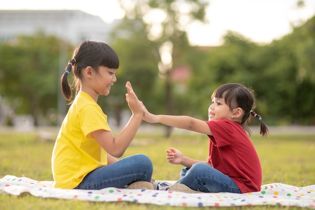 Zwei kleine Mädchen, die auf dem Gras im Park sitzen und Steinpapier-Scheren-Handspiel spielen