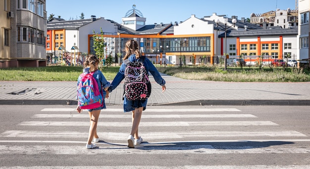 Zwei kleine Mädchen gehen zur Schule, Händchen haltend, Rückansicht.