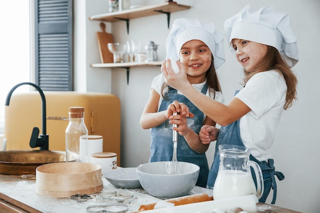 Zwei kleine Mädchen in blauer Kochuniform bereiten Essen in der Küche zu