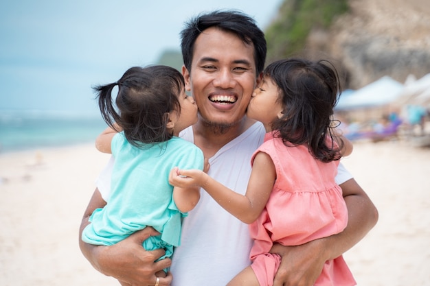 Zwei kleine Mädchen küssen sich zusammen zu seinem Vater am Strand