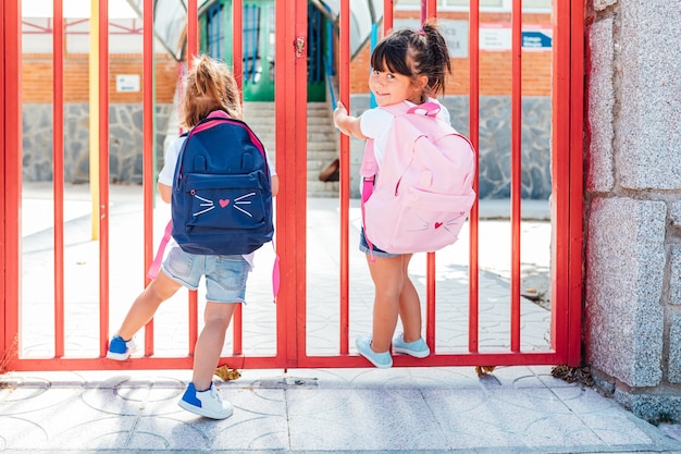 Zwei kleine Mädchen mit Rucksäcken an der Eingangstür der Schule