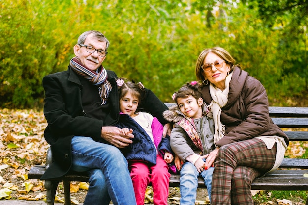 Zwei kleine Mädchen sitzen im Herbst Park mit ihren Großeltern auf einer Bank