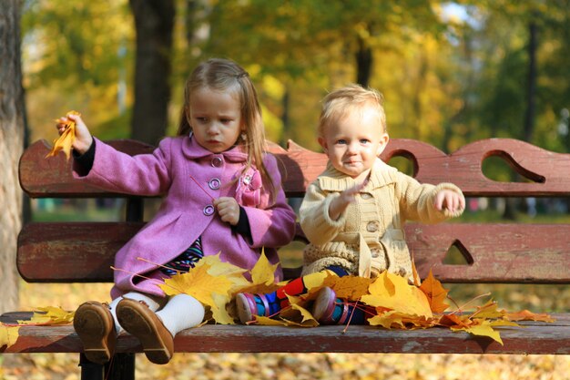 Zwei kleine schöne Mädchen, die auf der Bank am warmen Herbsttag sitzen