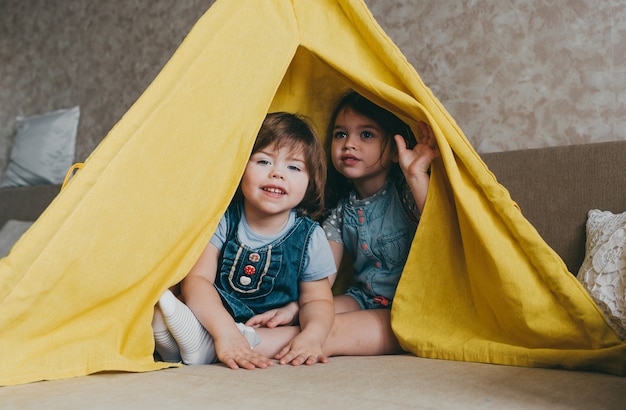 Zwei kleine schöne Mädchen spielen in einem gelben Tipi