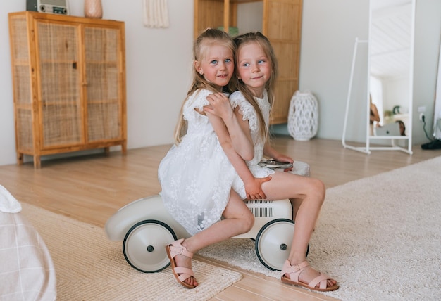 Foto zwei kleine schwedische schwestern sitzen auf einem spielzeugauto im wohnzimmer. kaukasische mädchen spielen zusammen