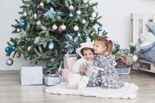 Zwei kleine Schwestermädchen öffnen morgens ihre Geschenke am Weihnachtsbaum