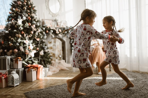 Zwei kleine Schwestern im Schlafanzug, die Spaß am Neujahrsbaum mit Geschenken haben