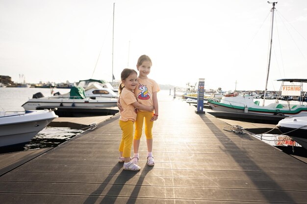 Zwei kleine Schwestern umarmen sich, während sie auf dem Pier stehen und den Sonnenuntergang am Meer genießen