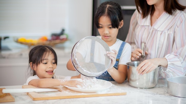 Zwei kleine süße asiatische Mädchen lernen mit einem neugierigen und glücklichen Lächeln, wie man Brot und Backwaren macht. Sie lernt und spielt