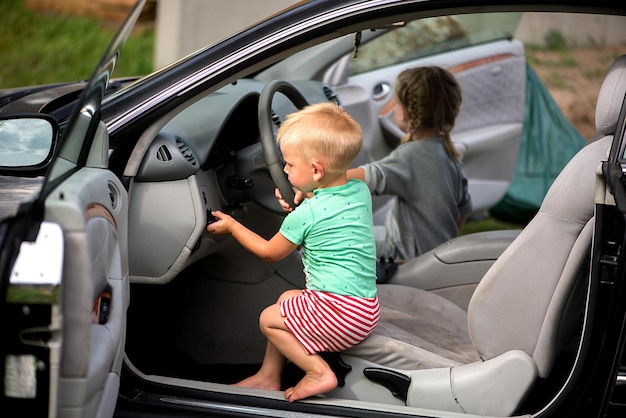 Zwei kleine süße Kinder, ein Bruder und eine Schwester, die im Auto am Steuer spielen