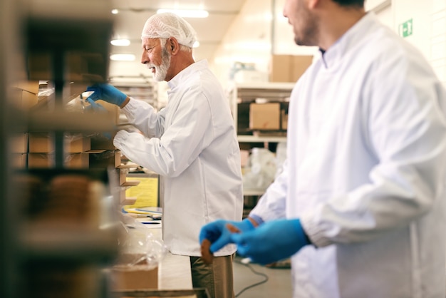 Zwei Kollegen, die Kekse in Kisten verpacken, während sie in der Lebensmittelfabrik stehen.