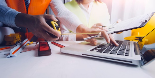 Zwei Kollegen diskutieren über Datenarbeit und Tablet-Laptop mit einem Architekturprojekt auf der Baustelle am Schreibtisch im Büro