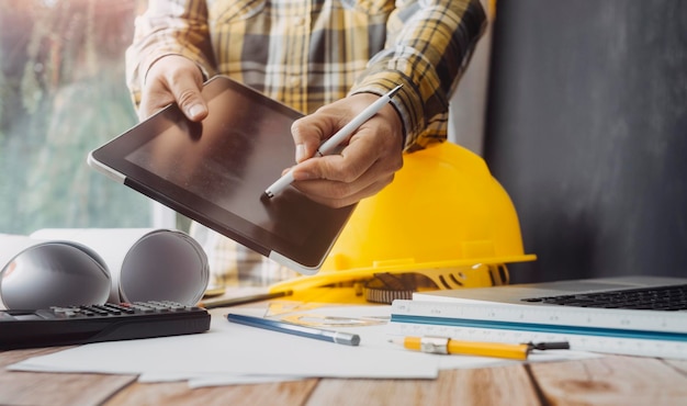 Zwei Kollegen diskutieren über Datenarbeit und Tablet-Laptop mit einem Architekturprojekt auf der Baustelle am Schreibtisch im Büro