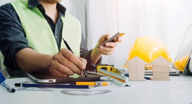 Zwei Kollegen diskutieren über Datenarbeit und Tablet-Laptop mit einem Architekturprojekt auf der Baustelle am Schreibtisch im Büro