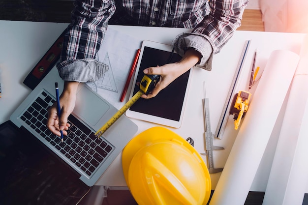 Zwei Kollegen diskutieren über Datenarbeit und Tablet-Laptop mit einem Architekturprojekt auf der Baustelle am Schreibtisch im Büro