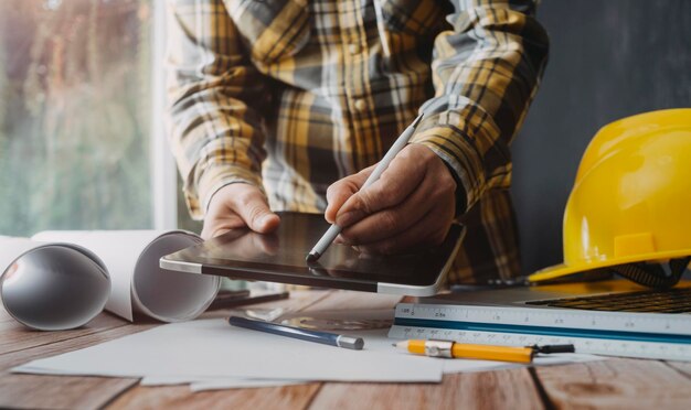 Zwei Kollegen diskutieren über Datenarbeit und Tablet-Laptop mit einem Architekturprojekt auf der Baustelle am Schreibtisch im Büro