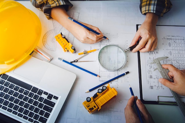 Zwei Kollegen diskutieren über Datenarbeit und Tablet-Laptop mit einem Architekturprojekt auf der Baustelle am Schreibtisch im Büro