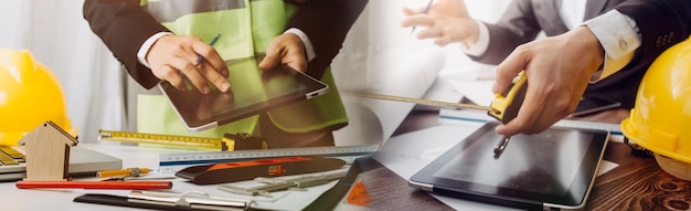 Zwei Kollegen diskutieren über Datenarbeit und Tablet-Laptop mit einem Architekturprojekt auf der Baustelle am Schreibtisch im Büro