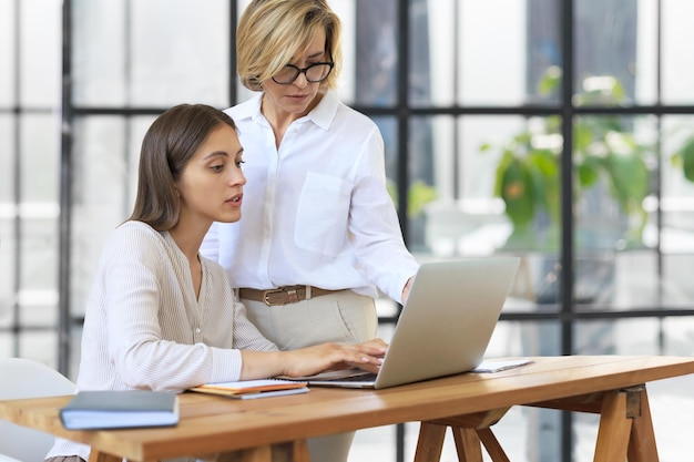 Zwei Kolleginnen, die mit Laptop arbeiten und neues Projekt besprechen