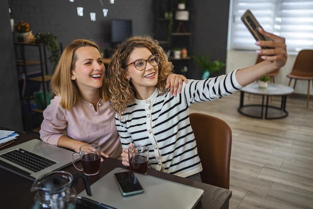 Zwei Kolleginnen machen Selfies und trinken Kaffee