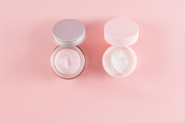 Zwei Kosmetikgläser mit einer zarten Creme zur Pflege junger Haut auf rosa Hintergrund Öffnen Sie das Glas Eine Kopie des Raumes Natürliche Kosmetik Top View