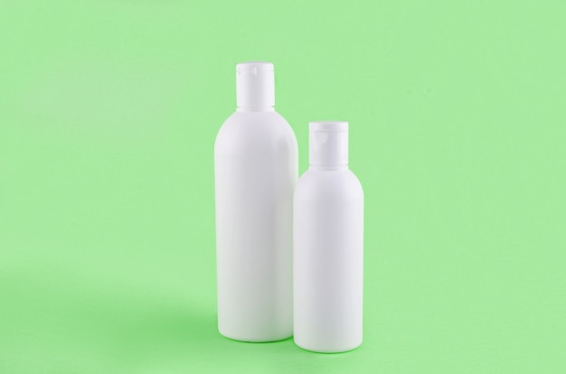 Zwei kosmetische Flaschen auf grünem Hintergrund. Set kosmetischer Produkte für Creme, Balsam oder Shampoo. Haar- oder Körperpflegekonzept. Minimale Szene mit leerem Platz für eine Unterschrift, Mock-up