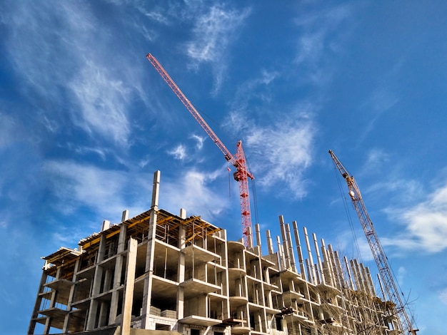 Zwei Kraniche, die Wohnhaus am Hintergrund des blauen Himmels des Tageslichts bauen. Baukonzept