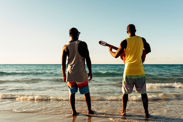 Zwei kubanische Freunde, die sich mit seiner Gitarre am Strand amüsieren. Freundschaftskonzept.